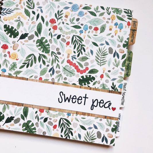Woodland cottagecore themed pregnancy journal. The cover is multi-colored and has muted tones. Mushrooms, caterpillars, and leaves are on the front cover. There is a personalization strip across the front and the journal is tabbed by trimester.